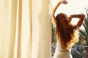 Young woman stretching arms, looking out window, rear view